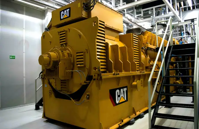 Gran generador eléctrico industrial CAT instalado en sala técnica con escaleras de acceso para mante